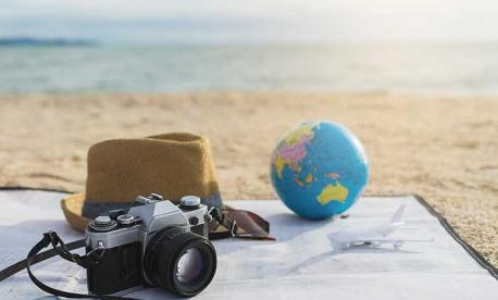Travel items on a beach including a camera, hat, globe and toy airplane, symbolizing global Passover 2026 destinations.
