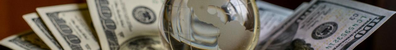 Glass globe resting on U.S. hundred-dollar bills symbolizing global Passover program prices and travel budgeting.