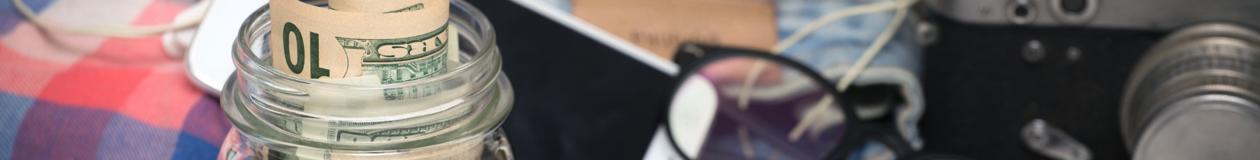 Travel savings jar with rolled dollar bills, map, camera, and travel accessories representing Passover program pricing and vacat